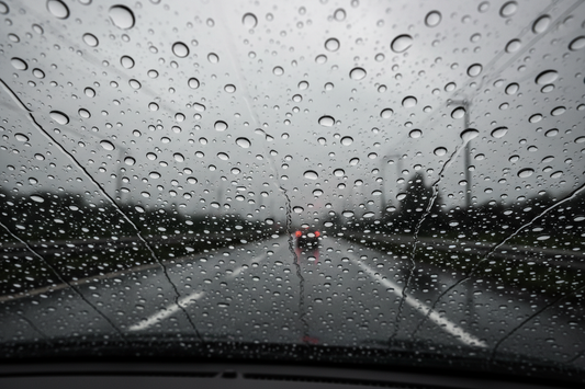 Water beading on a treated car windshield — large water droplets beading and rolling off a hydrophobic coated windshield at highway speed in rain