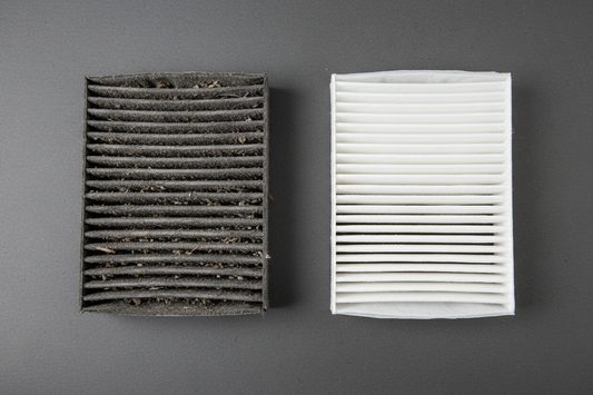 Car engine air filter housing open — black plastic rectangular air filter box with lid removed, dirty clogged paper air filter visible inside, intake hose connected to the side